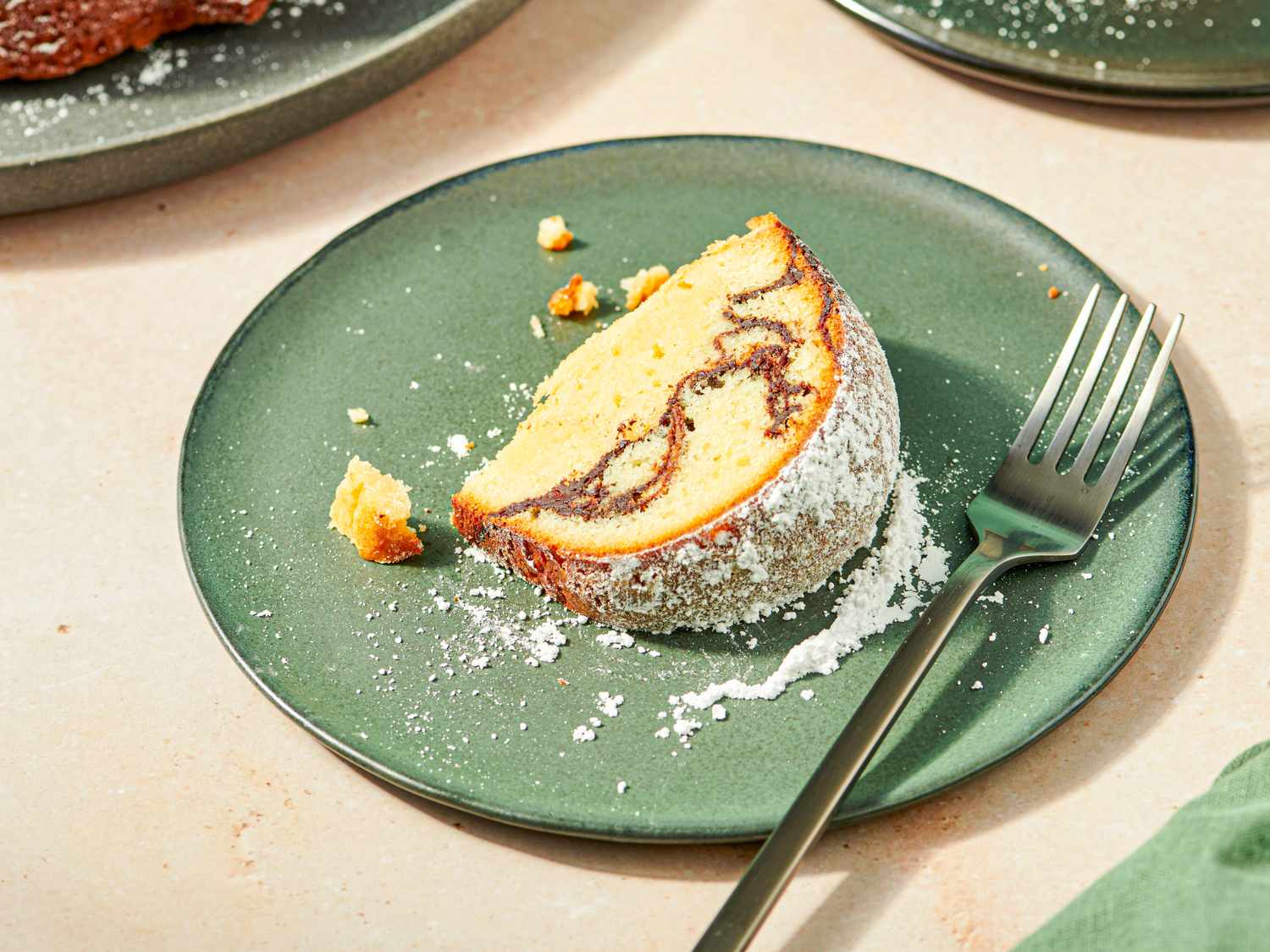 Slice of fluffy cake with a swirl dusted with powdered sugar on a green plate with a fork beside it