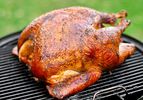 A golden Cajun-style turkey resting on the surface of a charcoal grill.