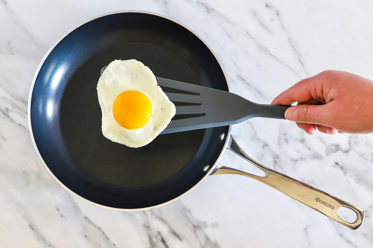 A fried egg on a spatula held above a Kyocera ceramic frying pan