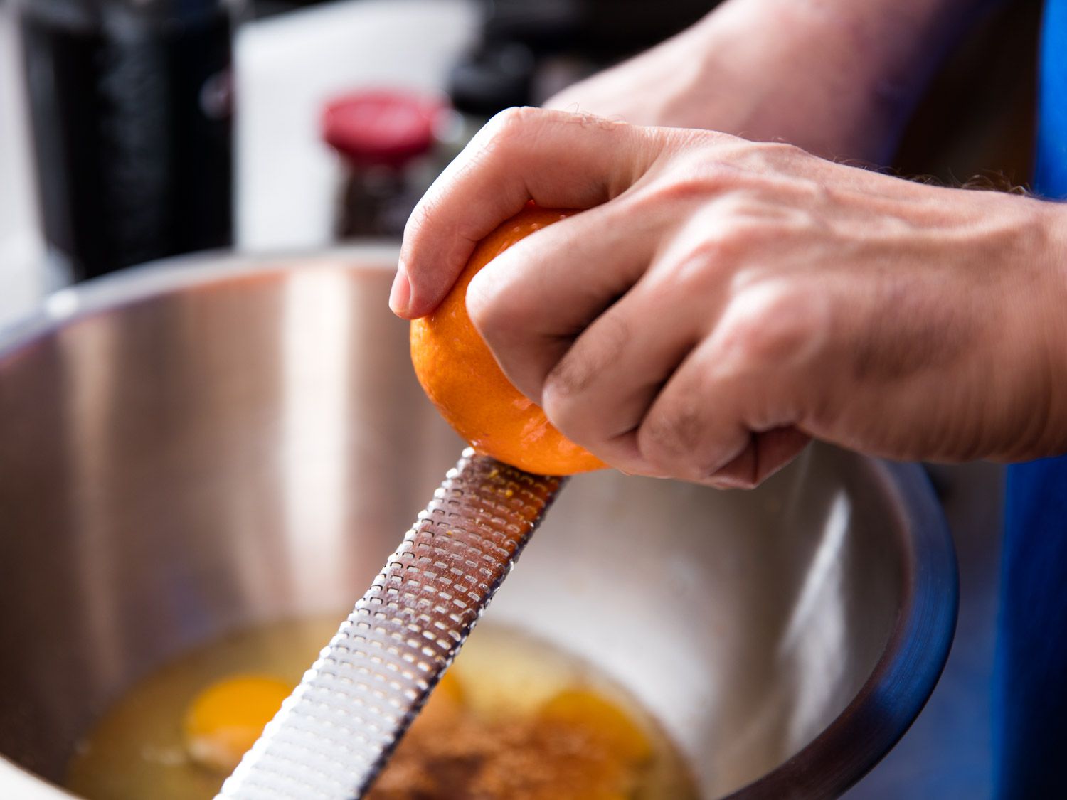 An orange is zested with a microplane over a mixing bowl.