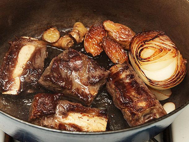 Close-up of browned short ribs and aromatics in the Dutch oven. The onions and ginger are nicely charred.
