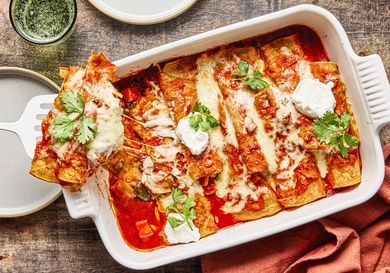 Freshly baked sweet potato enchiladas topped with melted cheese cilantro and dollops of cream served in a casserole dish