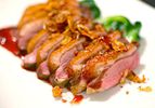 Sliced seared sous vide duck breast on a white plate with sauce and sautéed greens.