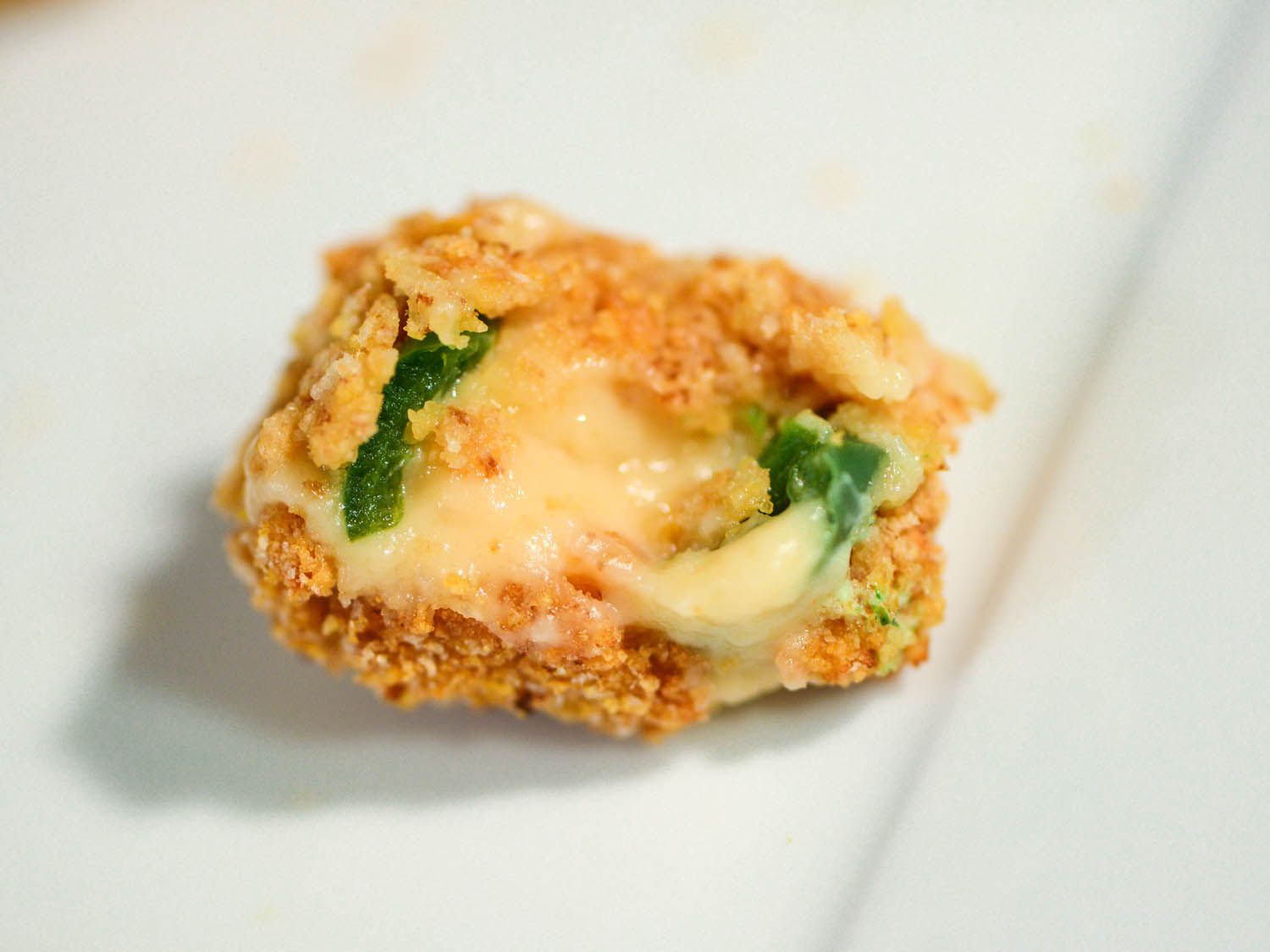 A half-bitten jalapeno popper, revealing its gooey interior. 