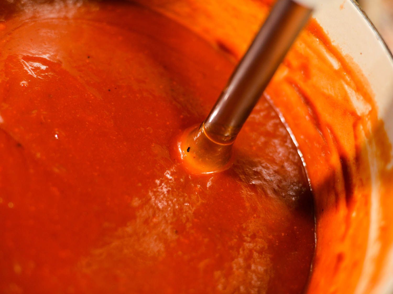 Closeup of the sauce being puréed with an immersion blender.