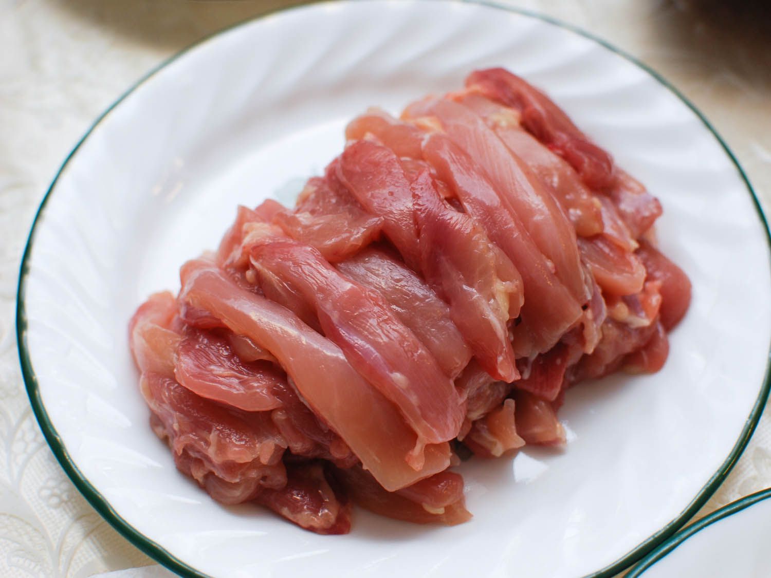 Strips of chicken meat on white plate for Chinese hot pot.
