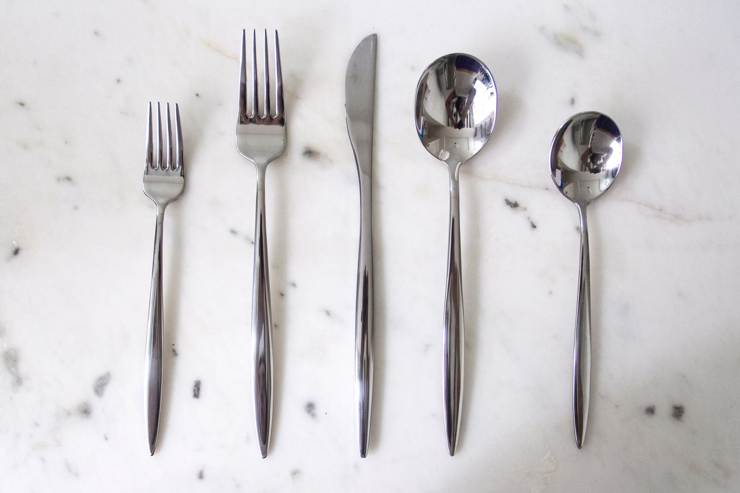 A set of five Fortessa flatware on a marble surface including two forks a knife a spoon and a smaller spoon