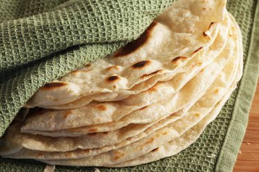 A stack of cook-and-serve flour tortillas wrapped in a green kitchen towel. 