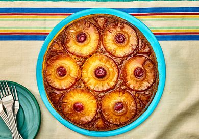 Overhead angle of pineapple upside down cake on a blue plate. The table cloth is a natural tone with blue, red, yellow and green stripes on the top. 