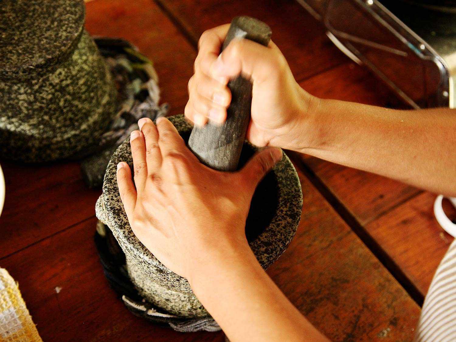 Hands pounding curry paste for Khao Soi Gai in a granite mortar and pestle.