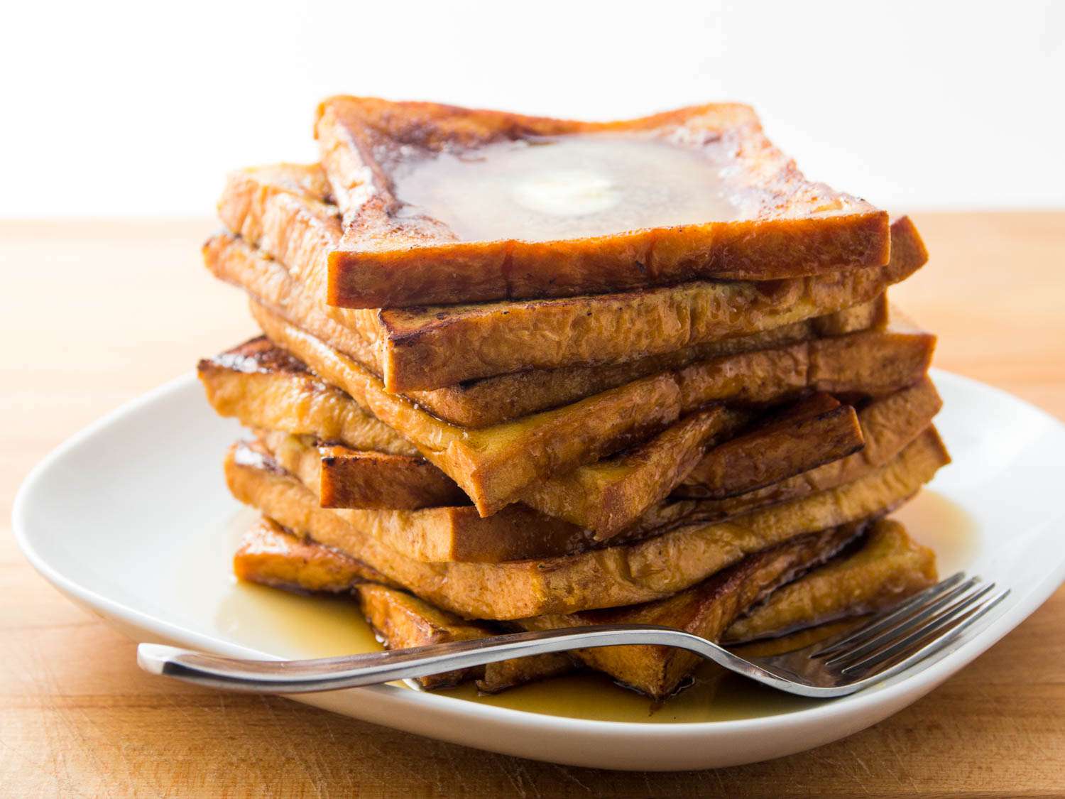 A stack of butter and maple syrup soaking french toast slices on a plate.