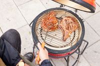 A person flips meat on the Kamado Joe KJ13RH 13.5 inch Joe Jr. Charcoal Grill