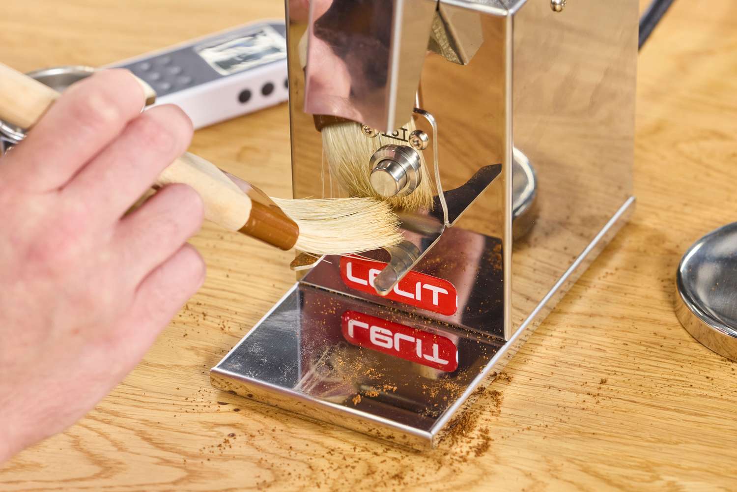 A hand using a brush to clean the Lelit Fred Tempo Burr Grinder