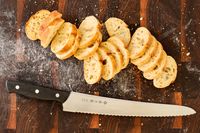 Sliced bread on a wooden cutting board with the Tojiro F-687 Hand Made Bread Knife