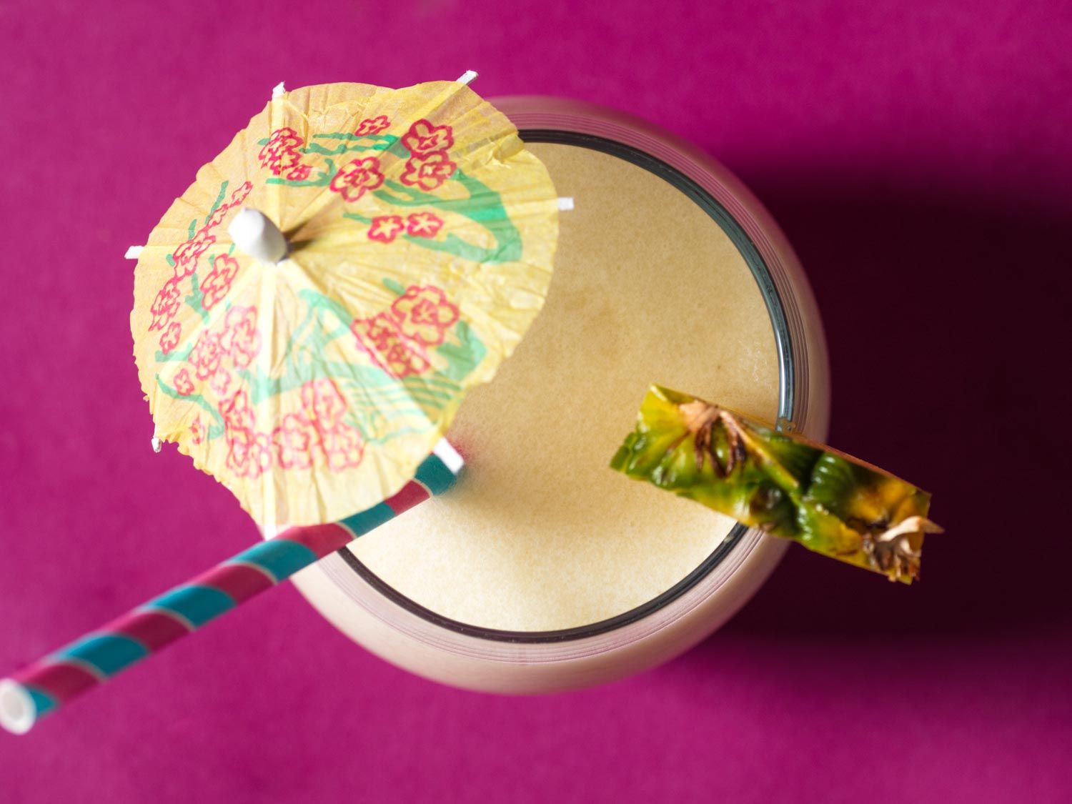 Overhead view of a piña colada with straw, umbrella, and pineapple garnish.