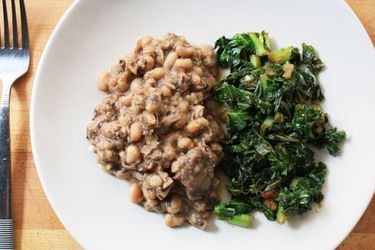 Overhead view of black-eyed peas with ham hock, served with a side of braised greens.