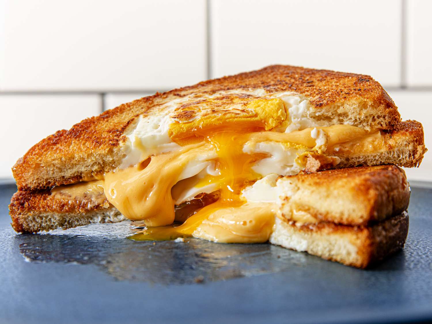 Two halves of a grilled cheese egg-in-the-hole sandwich stacked on top of each other, with cheese and egg overflowing from the middle. 