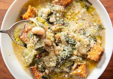 A bowl of zuppetta Scarola e Fagioli with croutons and beans a spoon scooping out the soup