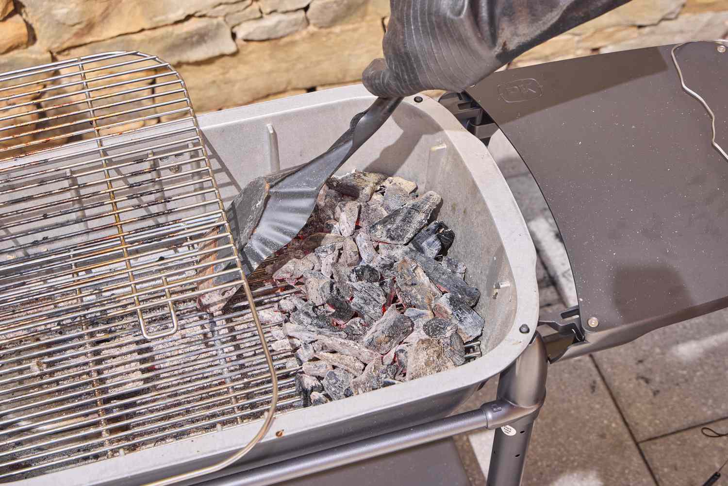 A hand using tools to move coals in the PK Grills Original PK300 Grill & Smoker 