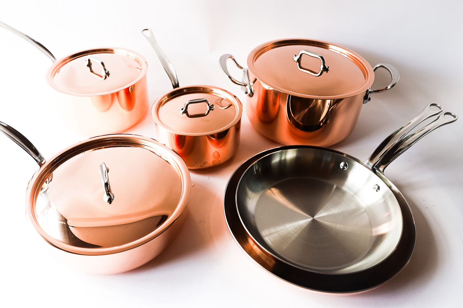 A collection of copper cookware including pots and pans with stainless steel interiors and lids