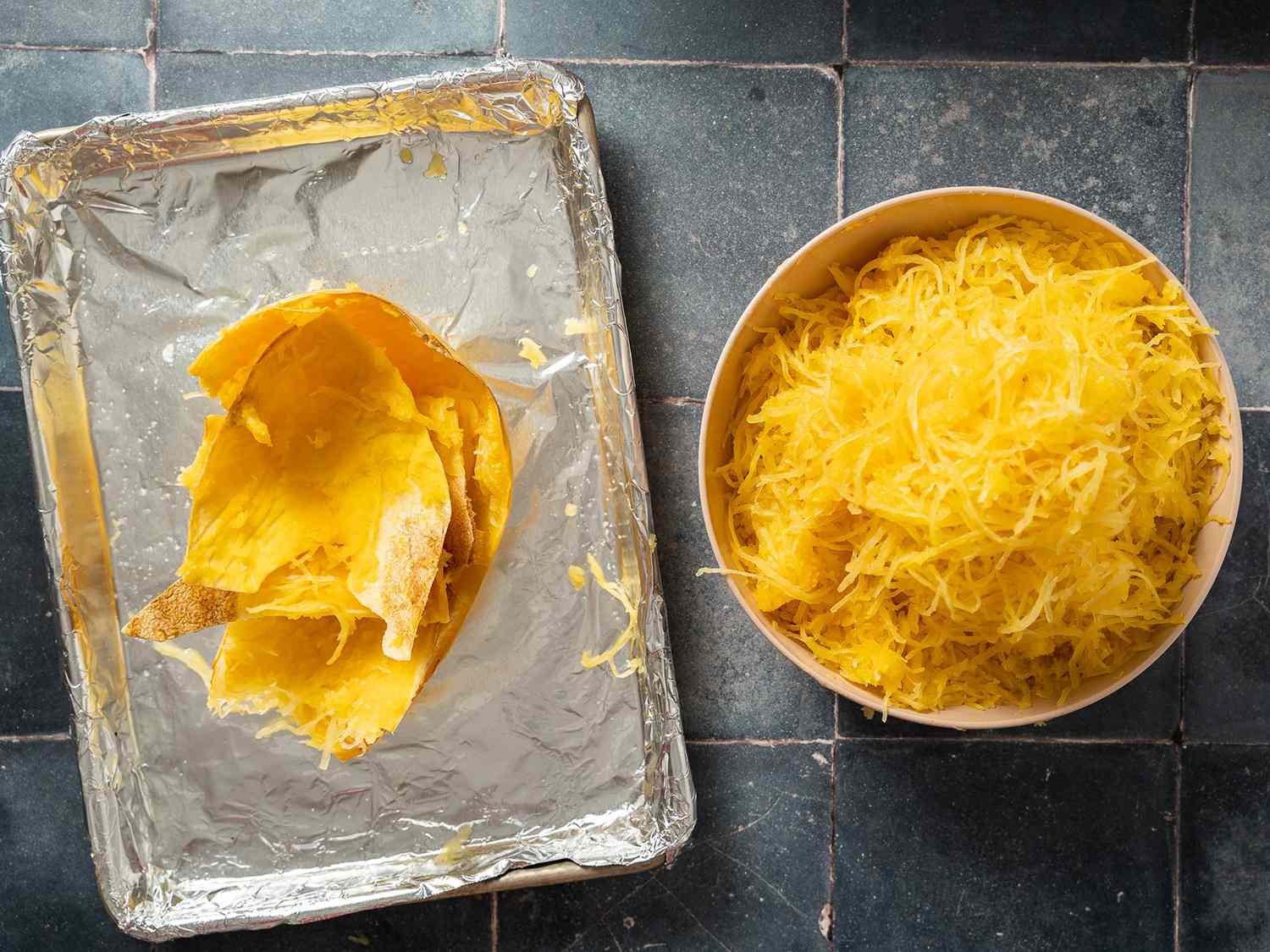 Shredded spaghetti squash in a bowl next to foil-lined roasting pan with discard squash skins