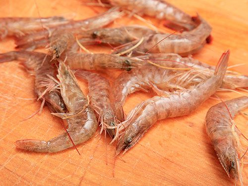 Raw whole head-on shrimp lying on a wooden cutting board. 