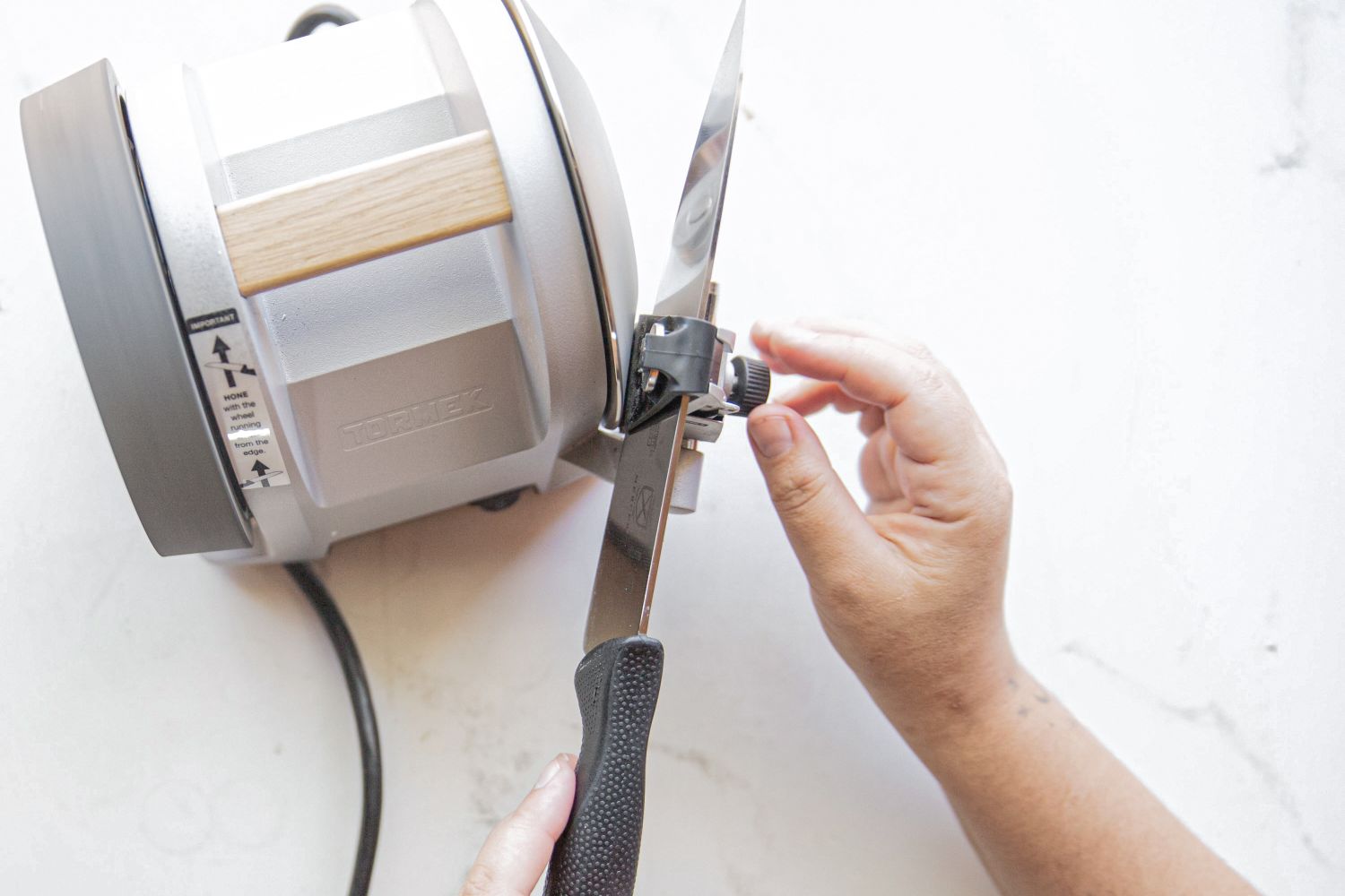 A person sharpening a knife using a Tormek sharpening machine hands adjusting the angle and position of the blade on the machine