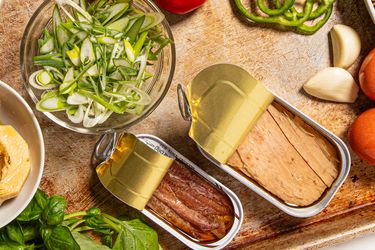 An assortment of sliced vegetables and opened cans of fish on a tray