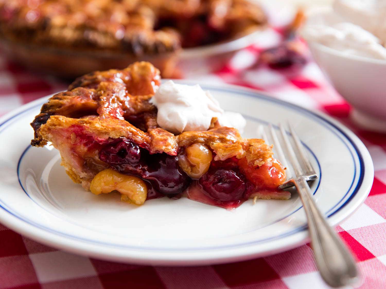 A slice of cherry pie topped with whipped cream on a white plate.