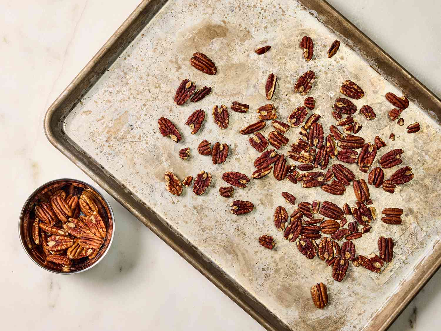 Sheetpan with toasted pecans on it and a small bowl of pecans on the side 