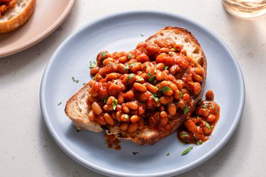 British-style baked beans on a piece of white bread which is placed on a blue ceramic plate on a stone background.