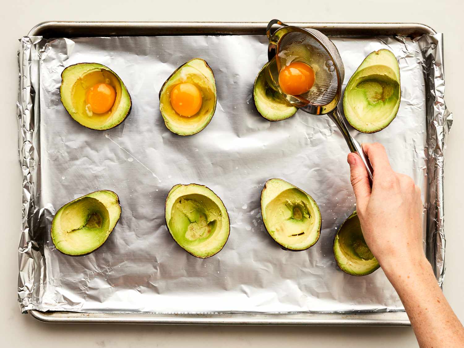 Placing eggs into avocados with a sieve