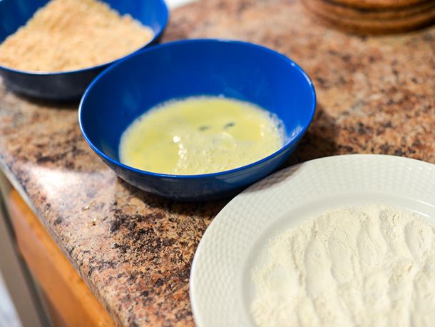 Dishes of breadcrumbs, beaten egg, and flour resting side-by-side on a countertop.