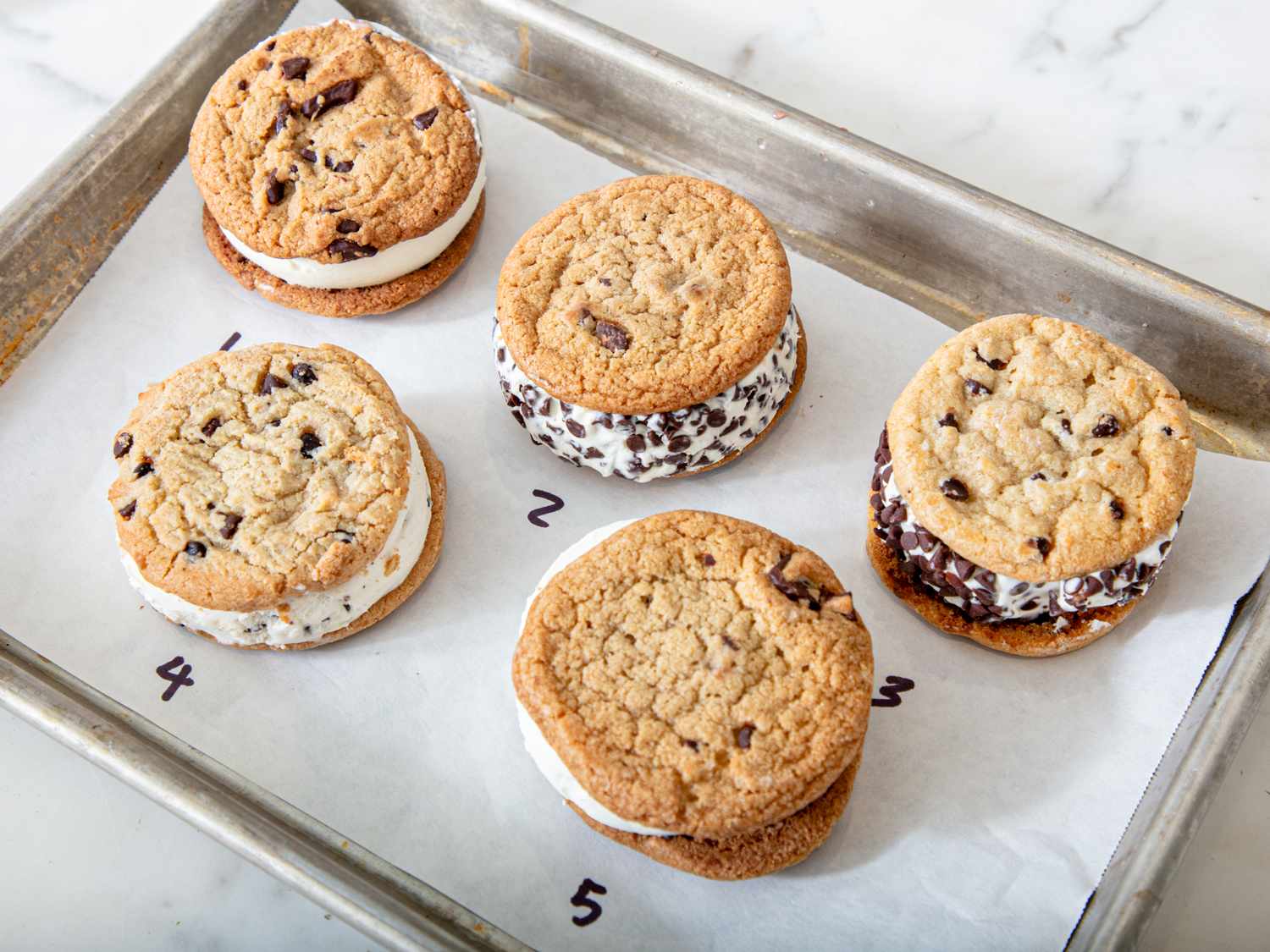 Five ice cream sandwiches arranged on parchment paper in a numbered order on a baking tray