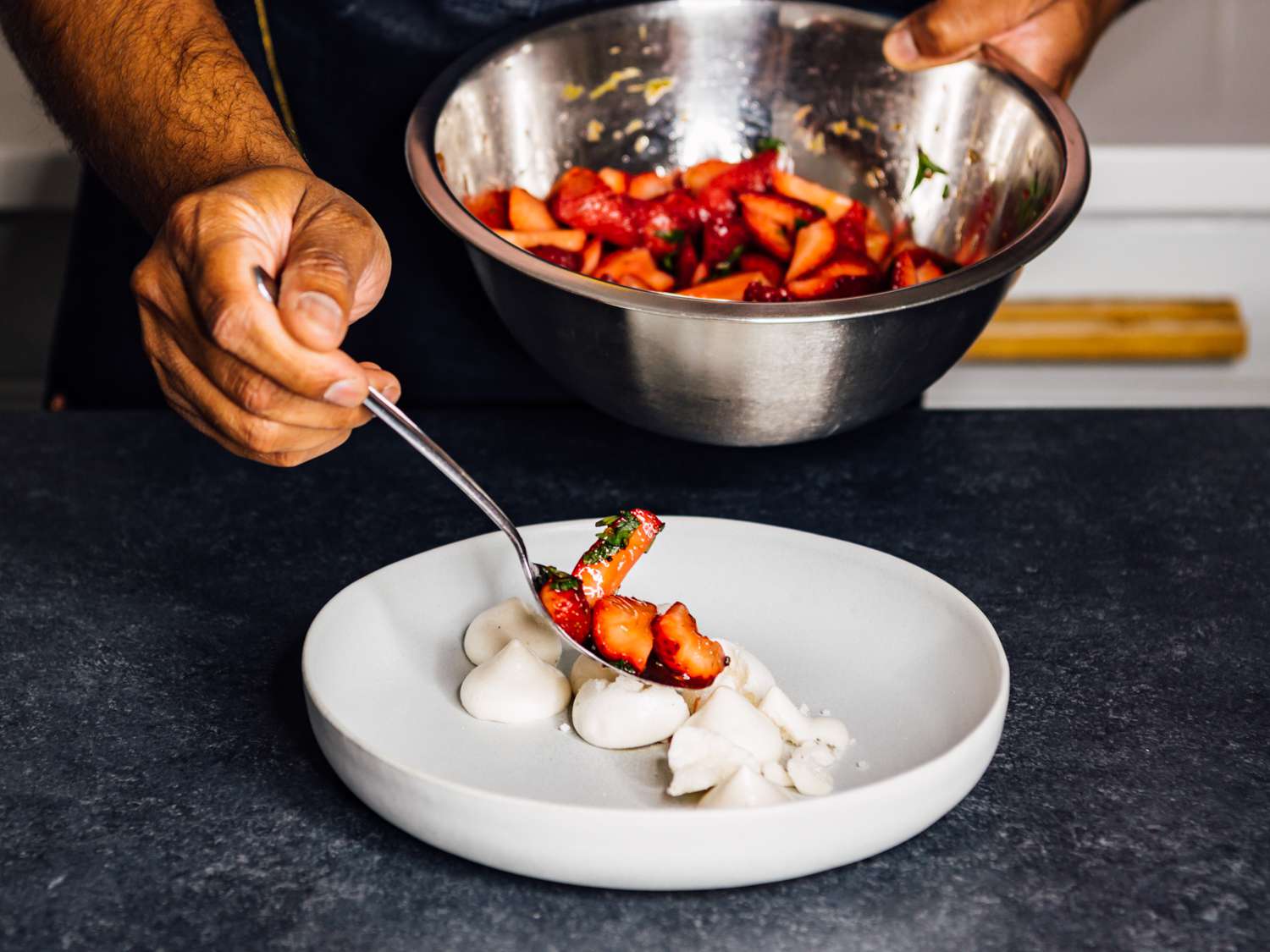 a hand spooning the strawberry compote onto the aquafaba meringue cookies on a plate