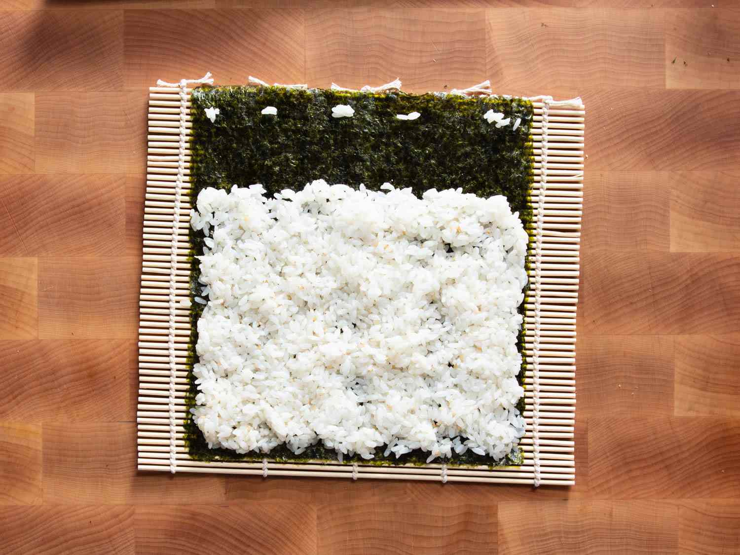 Overhead shot of sushi rice on seaweed resting on top of a bamboo rolling mat.