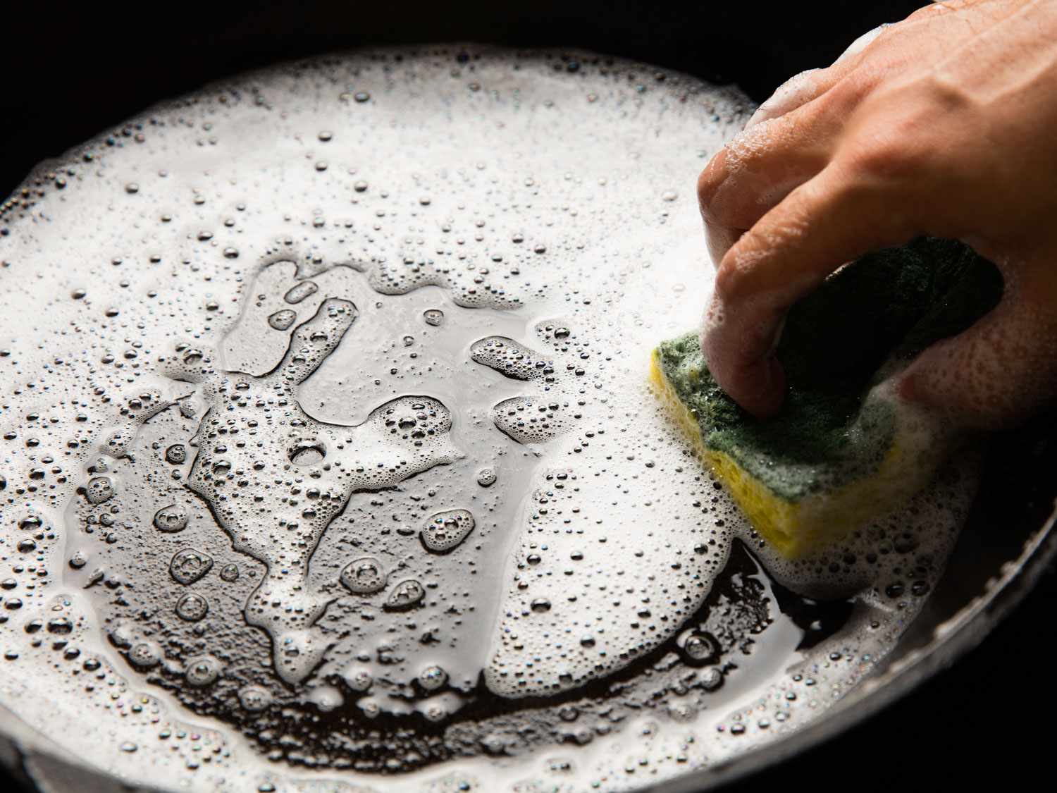 Cleaning a cast iron pan with warm, soapy water.