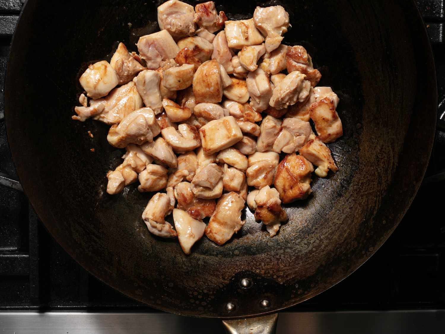 Stir-frying marinated chicken thigh pieces in a wok for takeout-style kung pao chicken.