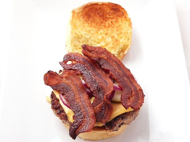 A cheeseburger assembled with three strips of bacon arranged next to one another.