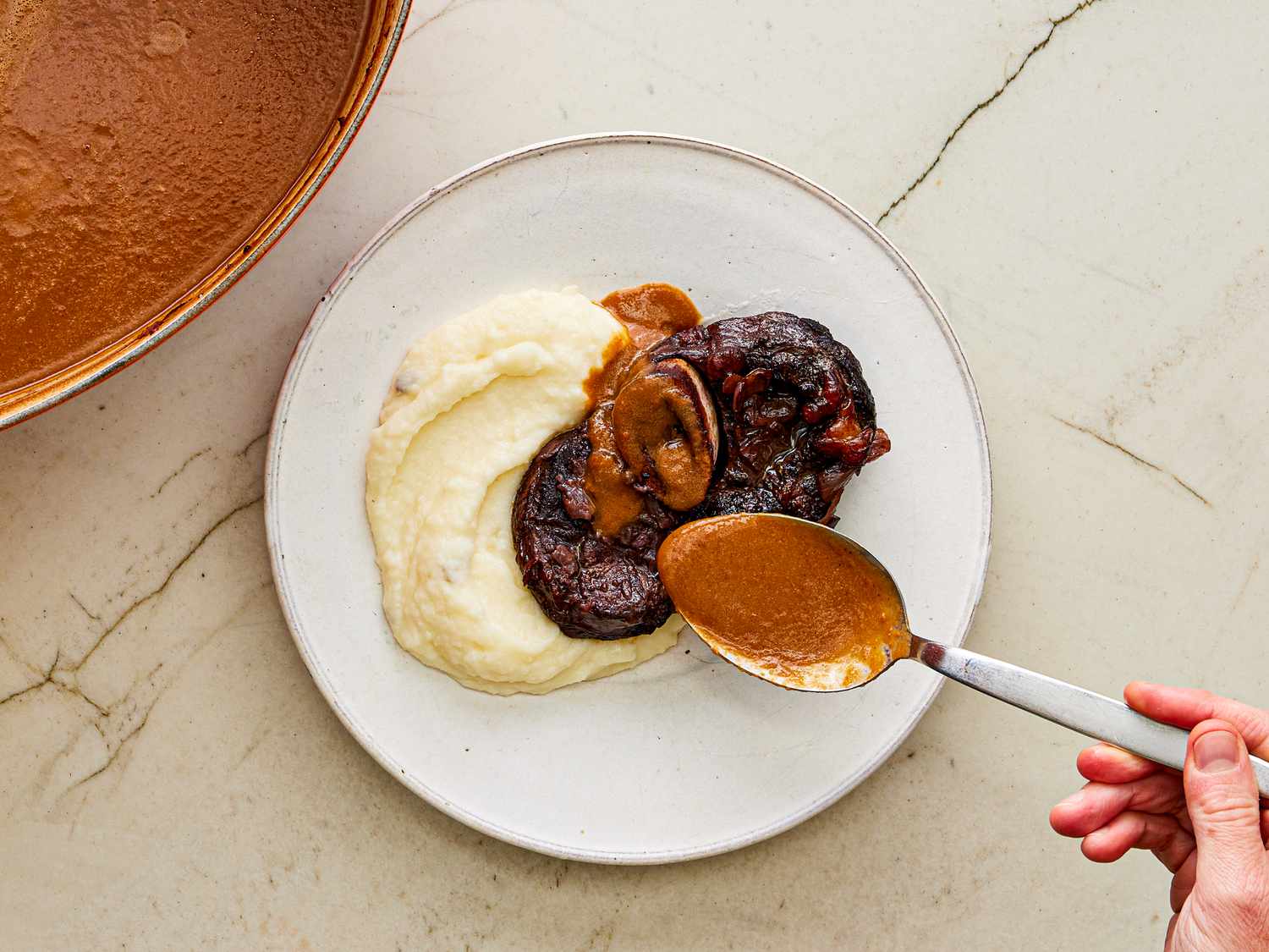 Overhead view of spooning sauce onto short ribs