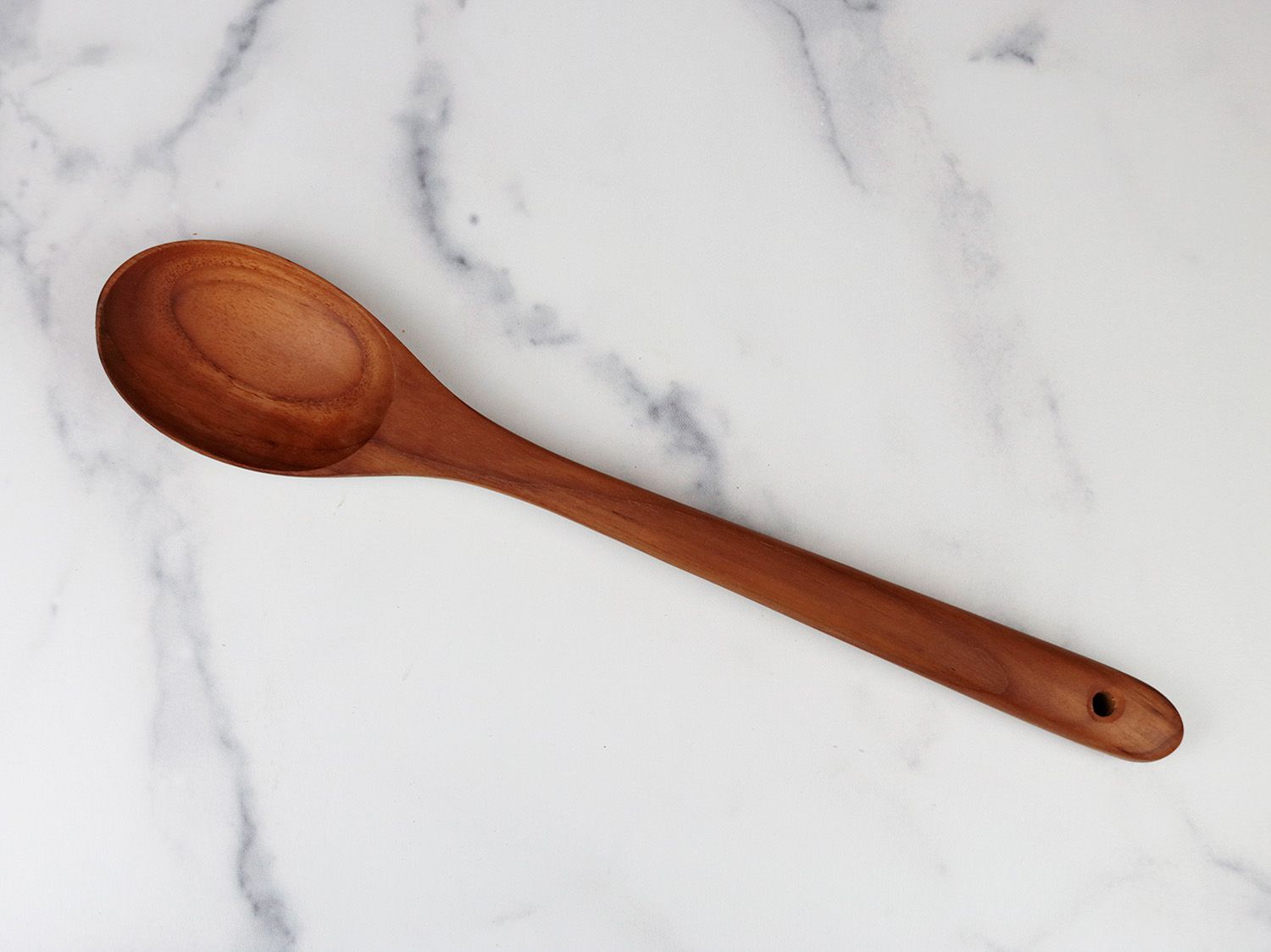 a wooden spoon with an oval head on a white marble backdrop 
