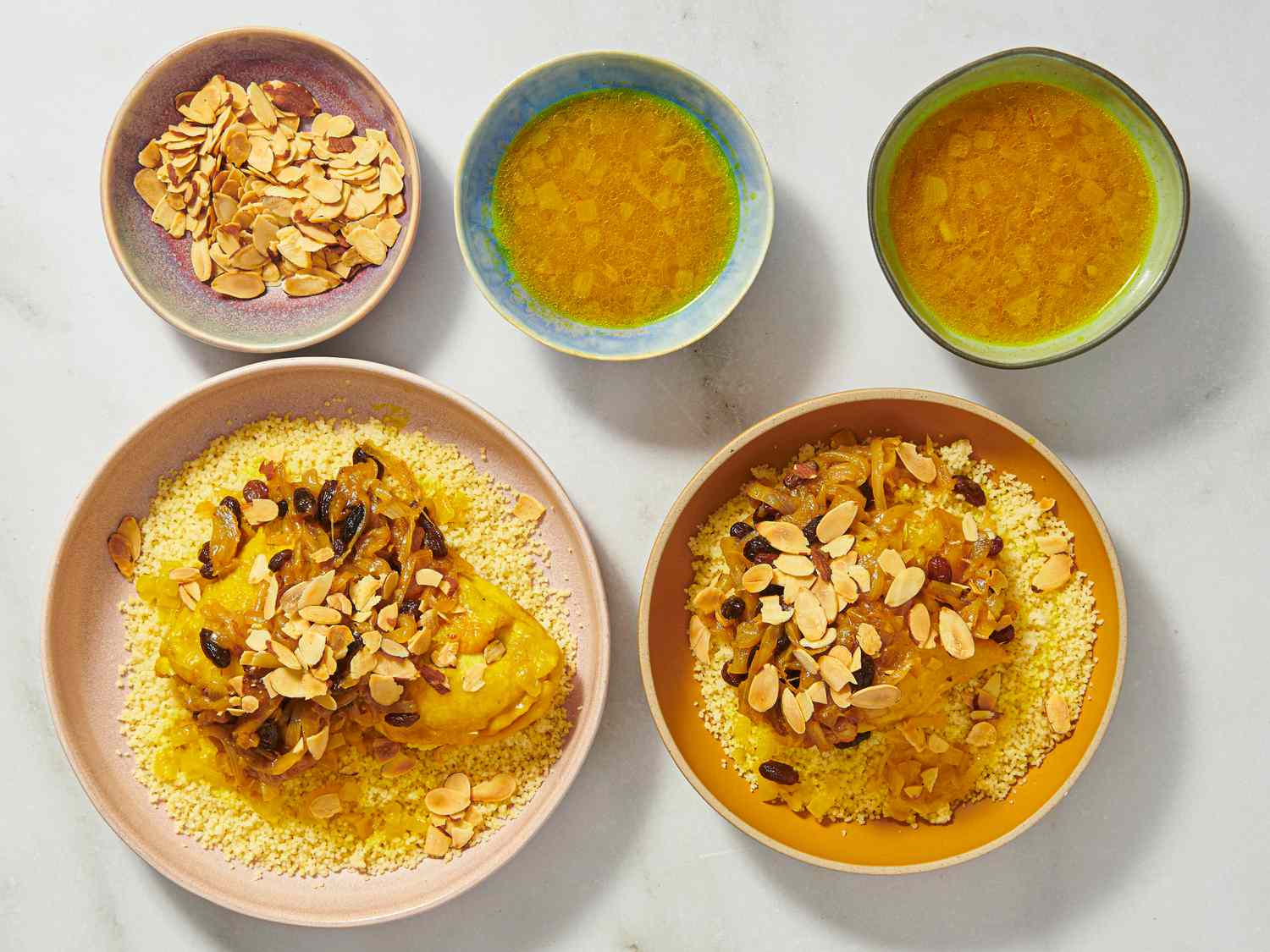 2 plates of Chicken Couscous T'faya with plate of almonds and 2 bowls of broth above them 