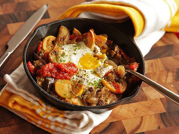 A cast iron skillet with eggplant, squash, and cherry tomato hash with baked eggs.