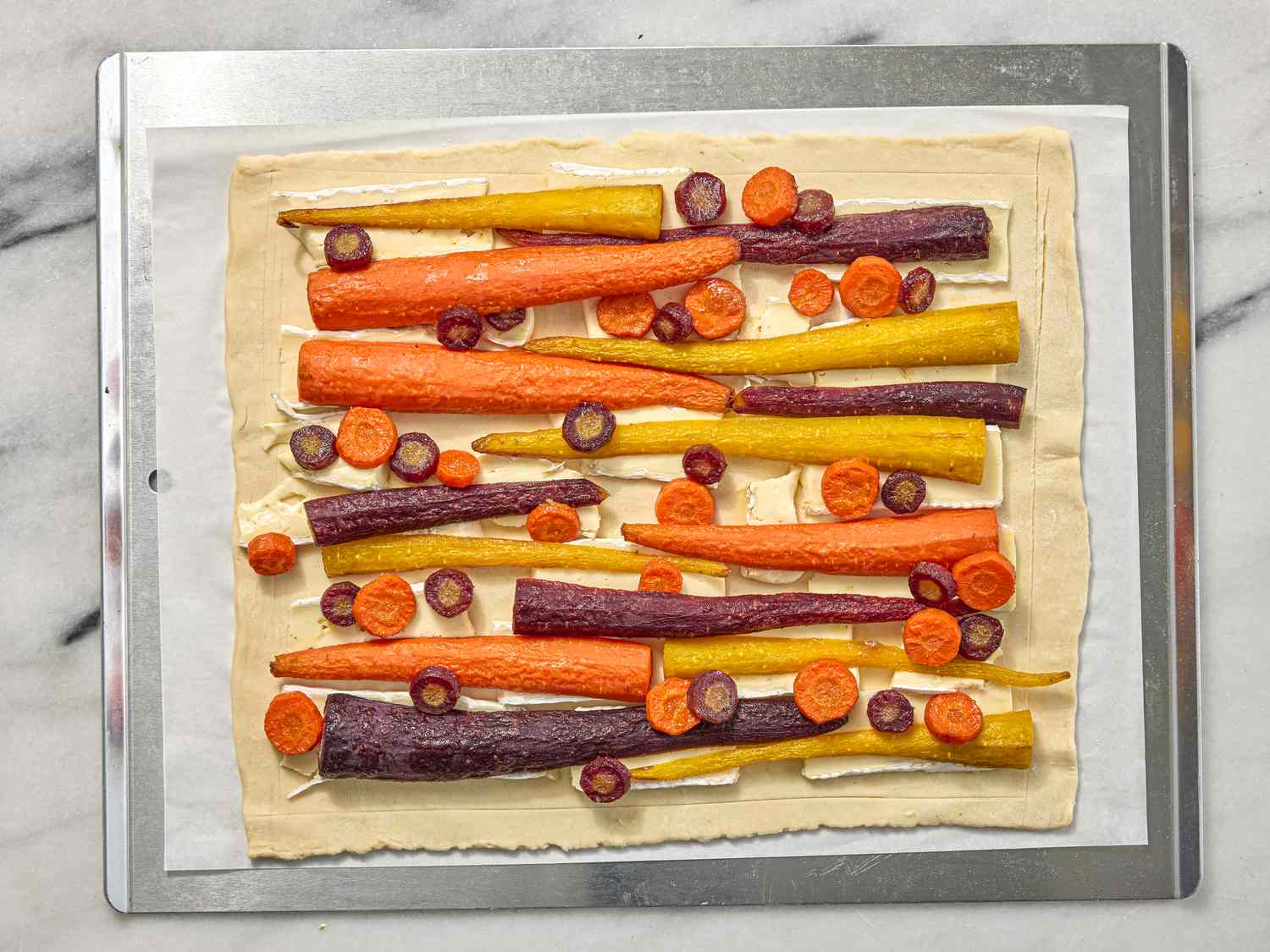 carrots and bire arranged on a dough on a sheetpan on a white marble surface 