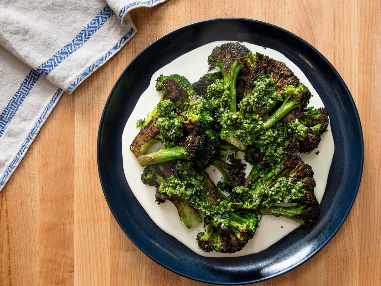 Overhead shot of serving platter with charred broccoli on top of cheese sauce with gremolata.