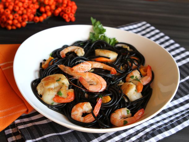A bowl of black squid ink pasta with shrimp and scallops on a black gingham patterned plate mat.