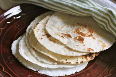 Finished gluten-free tortillas on a plate. A dish towel is nearby to cover the tortillas and keep them warm.