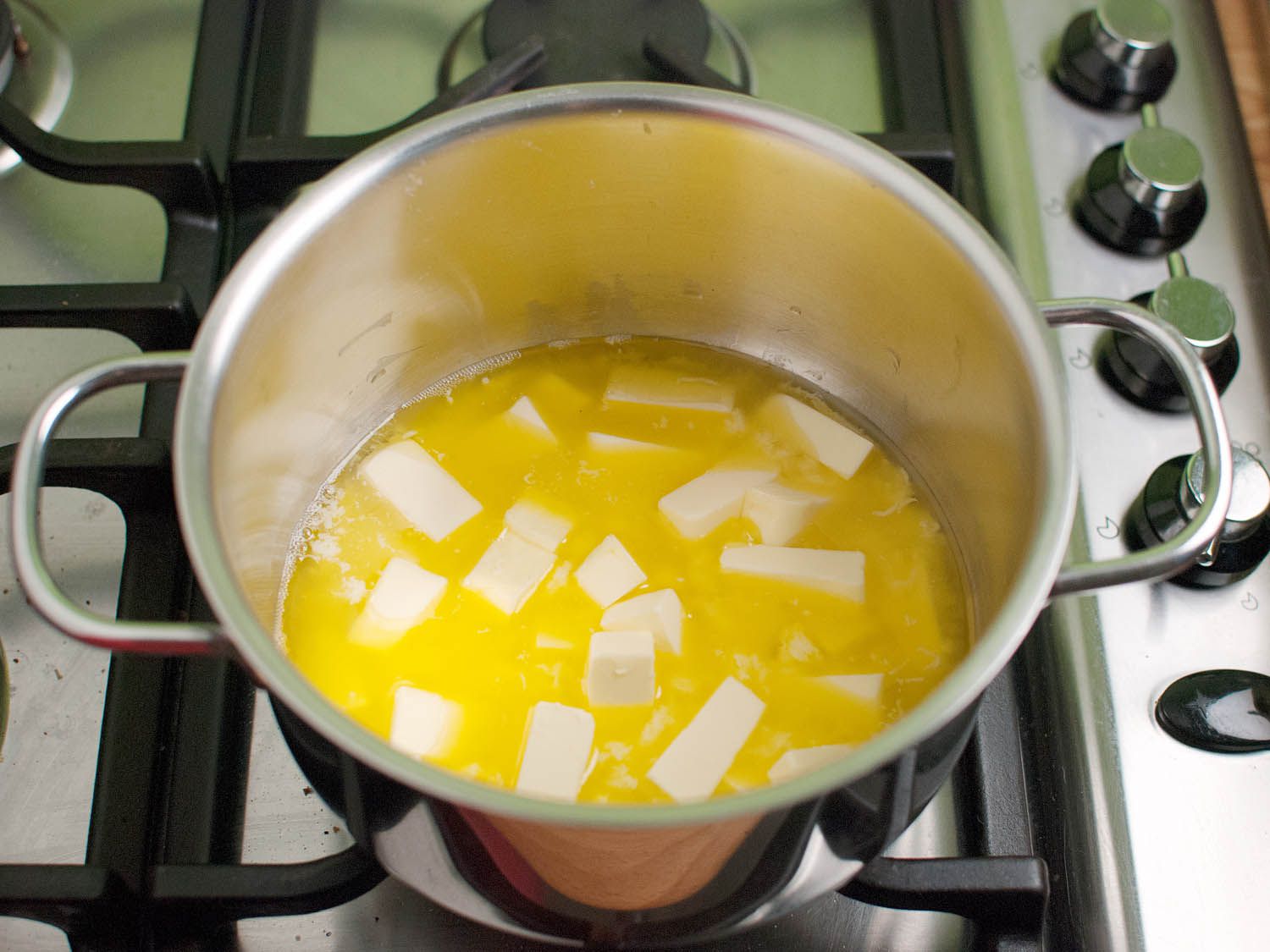 A large volume of butter partially melted inside of a metal pot set on a stove.