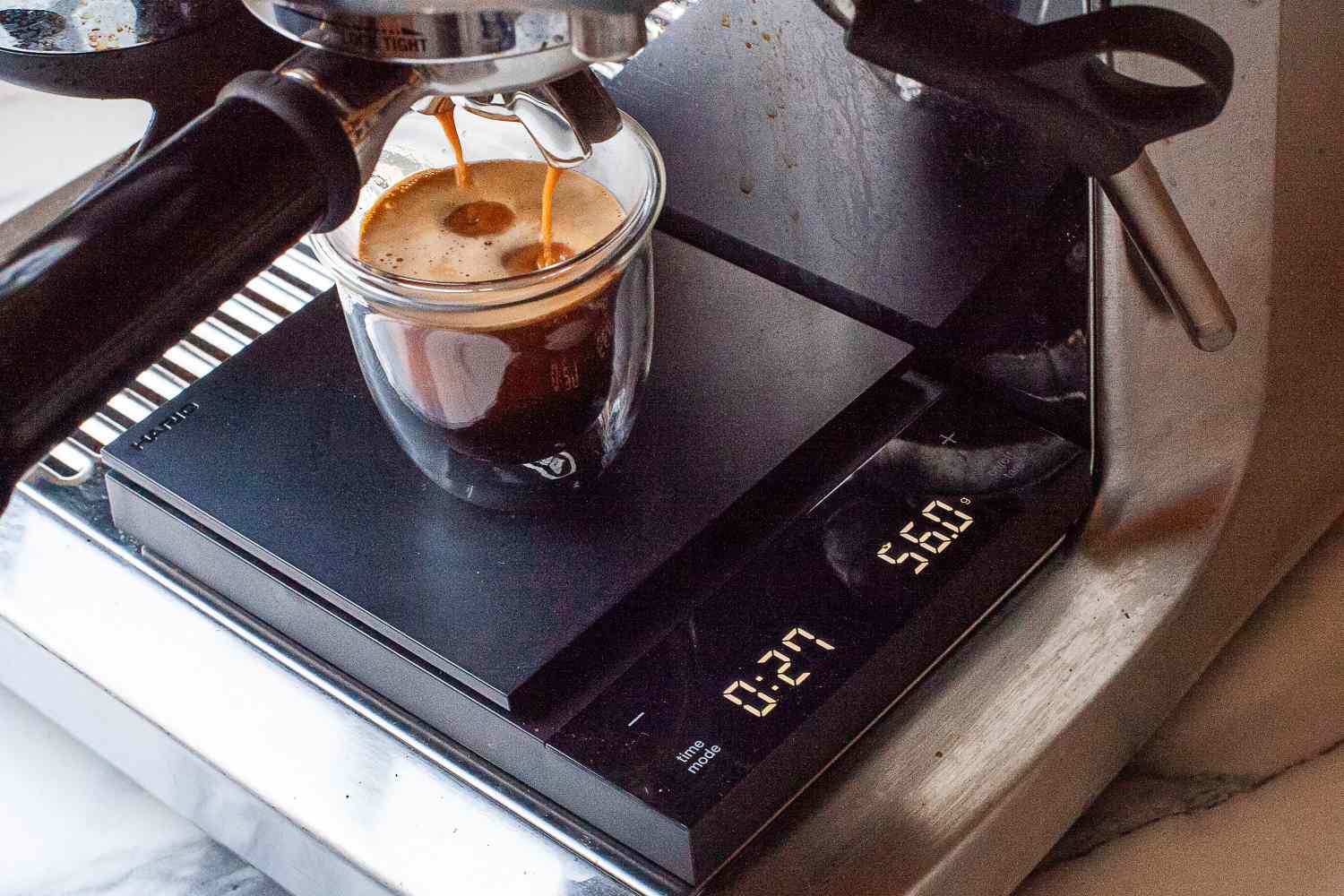 Espresso machine brewing into a glass placed on a Hario Polaris Coffee Scale displaying measurements
