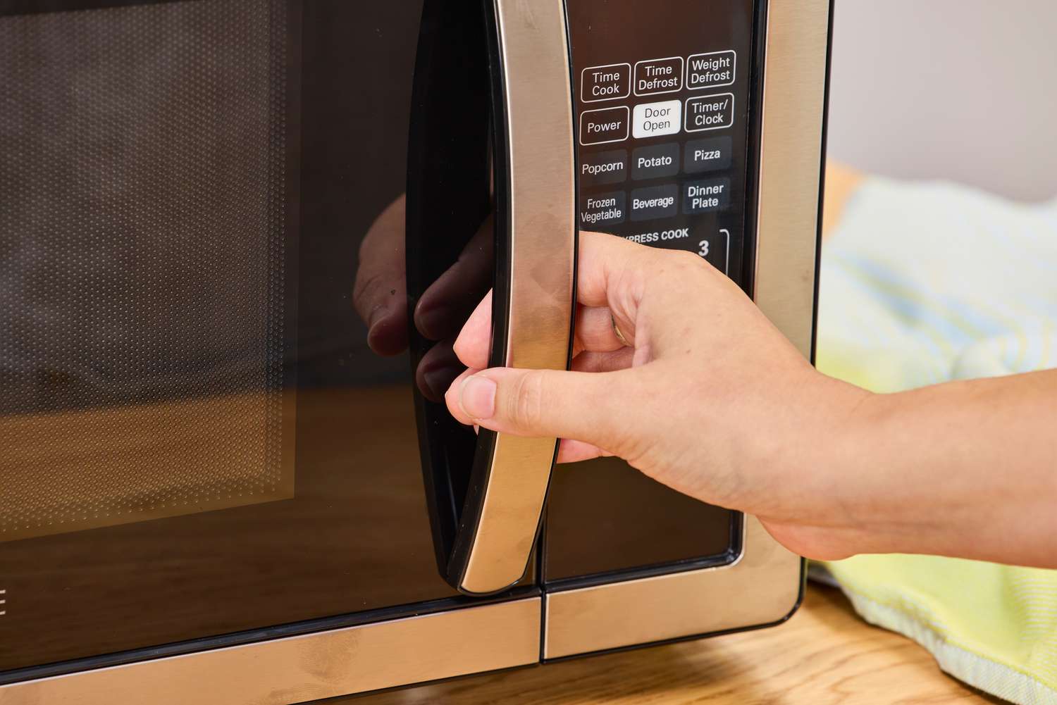 A hand holding the handle to the Farberware Countertop Compact Microwave (FMWO11AHTBKB) 